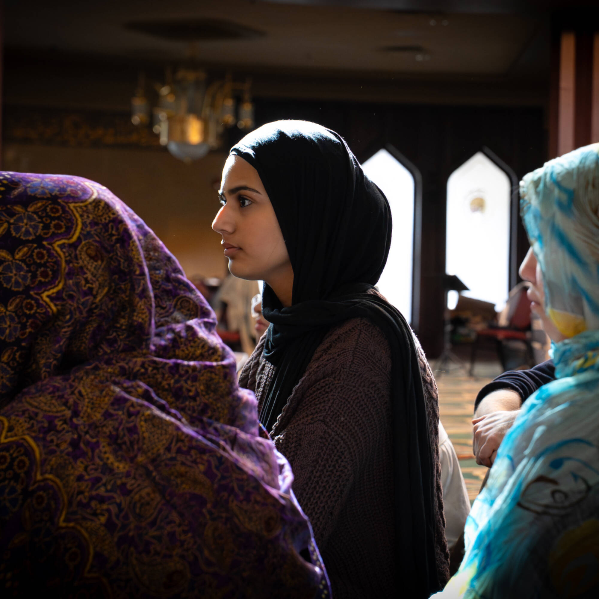 A girl in a black headscarf with two other students with headscarves in the foreground.